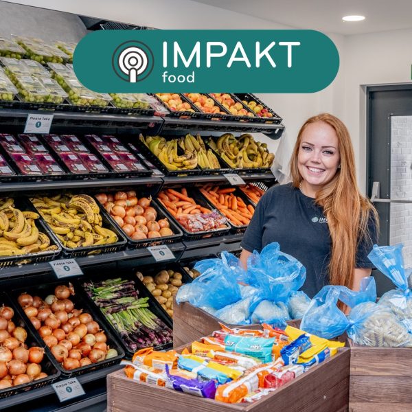 woman holding a range of food items against a backdrop of shelves of fruit with the IMPAKT logo above her